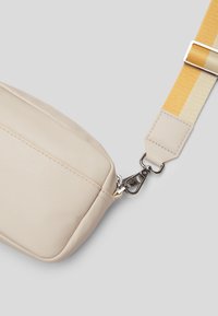 Beige nahka laukku, jossa on teksturoitu pinta, hopeinen klipsi ja raidoitettu hihna keltaisena ja valkoisena. Säädettävä hihnan pituus.