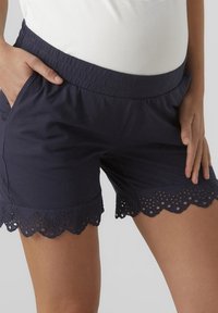 Tmavě modré šortky s elastickým pasem, zdobené vroubkovanou krajkovou lemovkou na spodním okraji a se dvěma bočními kapsami. Měkký, lehký materiál.