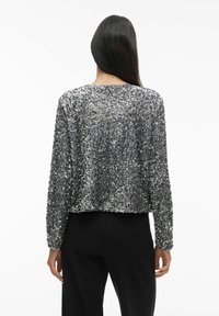 Srebrna bluzka z długim rękawem, o prostym kroju i okrągłym dekolcie, z miękką teksturą i metalicznym połyskiem na teksturowanej tkaninie.