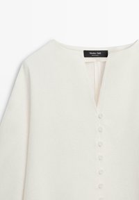 Biała bluzka z długim rękawem, okrągłym dekoltem, frontowymi guzikami obciągniętymi tkaniną oraz metką Massimo Dutti przy kołnierzyku.