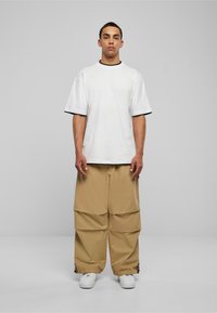 Vit kortärmad skjorta med svarta detaljer, i kombination med löst sittande beige cargo-byxor med vikdetaljer och snörning vid fållen. Vita sneakers.