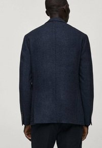 Granatowy wełniany żakiet o teksturowanej tkaninie, z pojedynczym rozcięciem z tyłu i mankietami na guziki. Dopasowany krój z gładkim wykończeniem.