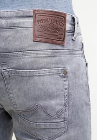 Ljusgrå denimjeans med en brun läderetikett märkt "Petrol Industries" på baksidan. Synliga sömmar och fickstygn.