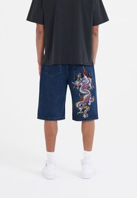 Denim shorts in dark blue with a dragon embroidery detail on the right leg. Features five pockets and a relaxed fit.