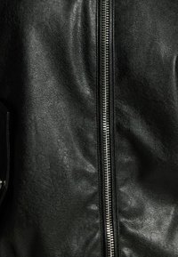 Svart läderjacka med en slät textur, framträdande silverdragkedja och subtila veck i tyget som ger extra djup.