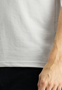 Helles graues Baumwoll-T-Shirt mit kleinem gesticktem Scherenlogo, kurzen Ärmeln und lässiger Passform. Weiche Textur mit minimalen Nähten.