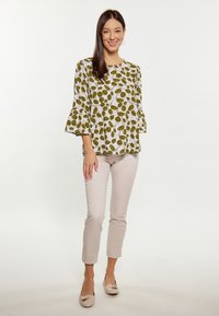 Bluză albă cu model de frunze verzi, cu mâneci evazate, asortată cu pantaloni bej deschis, ajustați, și pantofi neutri fără toc. Design simplu, textură ușoară.