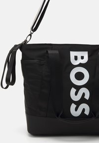 Fekete vászontáska tartós anyagból, nagyméretű fehér "BOSS" logóval, két strapabíró fogantyúval és egy kis oldalzsebbel.