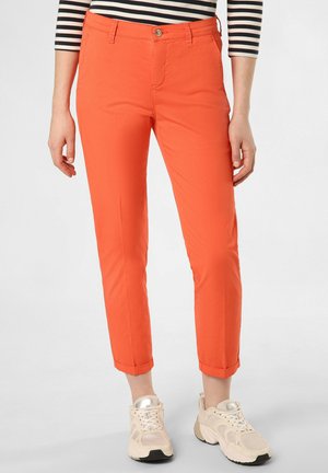 Frau trägt orangefarbene schmale, gekürzte Hose, cremefarbene klobige Turnschuhe und ein schwarz-weiß gestreiftes Oberteil mit Dreiviertelärmeln.