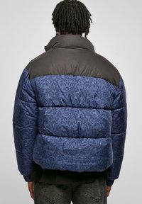 Modrá a čierna puffová bunda s kvetinovým vzorom na chrbte, vysokým golierom a prešívanými časťami pre izoláciu.