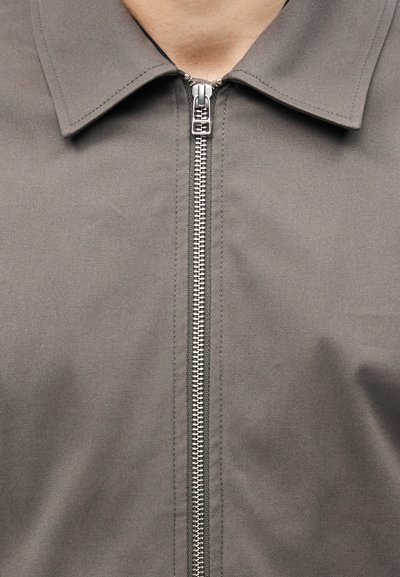 Κοντινή εικόνα ενός γκρι υφασμάτινου σακακιού με ασημένιο μεταλλικό φερμουάρ κλειστό και μυτερό γιακά.