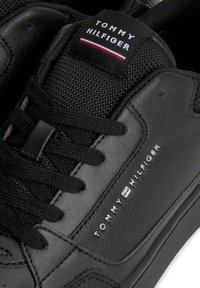 Musta lenkkari, jossa on sileä nahkapinta, tekstiilivivahteita ja mustat nauhat. Mukana brändätty kieli ja metallinen logo yksityiskohta sivussa.