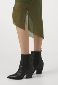 Svarta läderankelstövlar med spetsiga tår, kraftigare klackar och elastiska sidoinlägg. Designen har en slät textur och minimalistiska accenter.