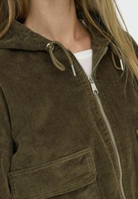 Brun kordflort zip-up jacka med huva, med en strukturerad yta, justerbar dragsko och framfickor. Silverfärgade detaljer.