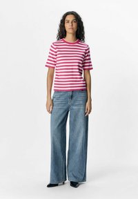 Chemise courte à manches courtes rayée rose et blanche avec un col rond, associée à un jean en denim bleu à jambes larges et des escarpins noirs à bout pointu.
