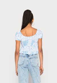 Blusa floral azul claro com mangas curtas bufantes e decote quadrado nas costas, ajustada na cintura, combinada com jeans de cintura alta.