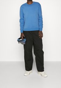 Ljusblå tröja med rund halsringning, bärs tillsammans med svarta cargobyxor. Modellen håller en liten metallisk blå påse. Sneakers är beige.