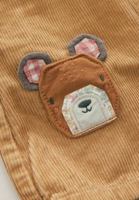 Il tessuto in corda marrone presenta un motivo di orso con orecchie texturate e dettagli a forma di toppe in rosa, grigio e accenti a fantasia.