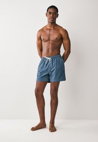 Muške kupaće hlače u tamnoplavom materijalu, s elastičnim pojasom i bijelim vezicama, te jednostavnim i elegantnim dizajnom.