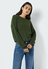 Mørkegrønn ribbestrikket genser med rund hals og oversized ermer, kombinert med lyseblå rette jeans. Strukturert strikket stoff.