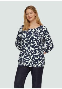 Navyblauw langekorte top met witte abstracte vogelpatronen, met een brede halslijn en een relaxte pasvorm, gecombineerd met donkere jeans.