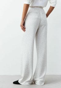 Hellgraue Jogginghose mit weitem Bein aus einem weichen, strukturierten Stoff. Verfügt über einen hohen Bund und zwei Gesäßtaschen für zusätzliche Funktionalität.