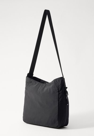 Sac à épaule en nylon noir avec une texture douce et rembourrée, un dessus angulaire, une sangle ajustable et une poche zippée sur le côté.
