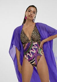 Bikini con top a stampa leopardata e parte inferiore alta a motivi colorati, sovrapposto a un kimono trasparente viola.