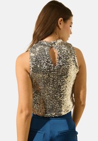 Top sans manches en sequins argentés et dorés avec un col rond et un détail en trou de serrure au dos. Texture lisse, design ajusté.