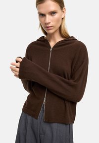 Brązowy zip-up hoodie wykonany z miękkiego materiału, z kapturem i długimi, luźnymi rękawami. Wyjątkowy srebrny zamek błyskawiczny z przodu.