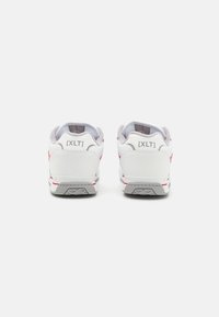 Hvide sneakers med grå accenter, der har en tekstureret sål, iøjnefaldende røde detaljer og fremtrædende branding på hælen. Bagfra.