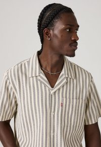 Short-sleeve button-up shirt featuring vertical navy and cream stripes, a chest pocket, and a Levi's logo tag on the pocket.