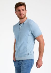Camisa polo de color azul claro con mangas cortas, tejido texturizado, cuello y dobladillo acanalados, tapeta de tres botones y detalles de rayas verticales.