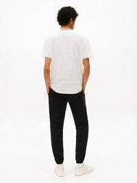 Weißes Baumwoll-T-Shirt kombiniert mit schwarzen Jogginghosen. Die Jogginghosen haben elastische Bündchen, während die Sneaker weiß mit strukturierten Details sind.