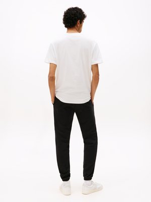 Witte katoenen T-shirt gecombineerd met zwarte joggingbroeken. De joggingbroeken hebben elastische boorden, terwijl de sneakers wit zijn met een gestructureerd detail.