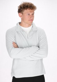 Hellgrauer Reißverschluss-Fleece-Pullover mit hohem Kragen, langen Ärmeln und weicher Textur, getragen über einem weißen, locker sitzenden Shirt.