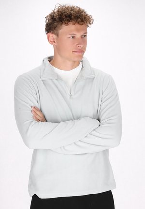Lys grå zip-up fleece pullover med høj krave, lange ærmer og en blød tekstur, båret over en hvid skjorte med en afslappet pasform.
