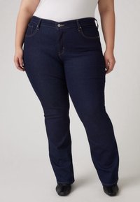 Jeans en denim bleu foncé avec une coupe droite, poches avant, et une fermeture à bouton. Le tissu semble lisse avec des détails de couture.