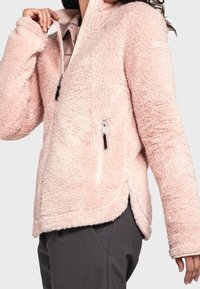 Jasnoróżowa polarowa kurtka z zamkiem z przodu, bocznymi kieszeniami i miękkim, teksturowanym wykończeniem. Posiada luźny krój i zaokrąglony dół.