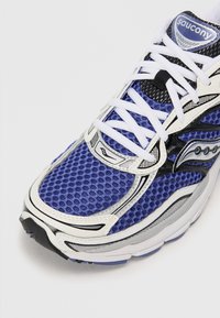 Blue and black athletic shoe with mesh upper, white laces, padded tongue, and silver accents. Rounded toe and textured sole.