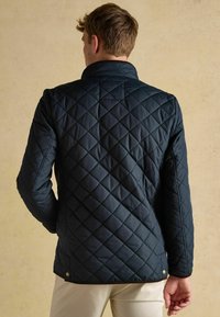 Námořnická prošívaná bunda s vysokým límcem, diagonálním prošíváním a zapínáním na patentky na lemu. Hladká látka s mírným leskem, přizpůsobený střih.