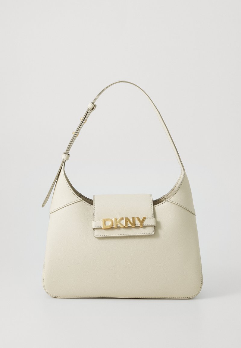 Bežinė odinė rankinė, turinti struktūrinę formą, vieną rankeną, magnetinį uždarymą ir aukso spalvos „DKNY“ logotipą priekyje. Lygus paviršius.