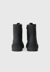 Bocanci negri până la gleznă, cu o textură netedă și un design căptușit, dotati cu un fermoar pe lateral și o talpă groasă pentru un plus de înălțime și stabilitate.
