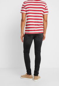 Camiseta a rayas rojas y blancas con mangas cortas, combinada con jeans negros ajustados y zapatillas de color beige claro. Fondo liso.