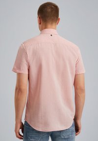 Camisa de manga corta, color rosa claro, con cuello, textura suave, dobladillo curvado y un pequeño logo en la parte posterior. Combinada con jeans.