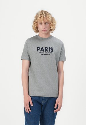 T-shirt in cotone grigio con una scritta audace "PARIS" in blu sul davanti. Collo rotondo e maniche corte. Indossato con jeans in denim blu.