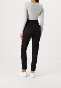 Zwarte slim-fit broek met een hoge taille, gemaakt van gladde stof. Gecombineerd met een aansluitend grijs langemouwen shirt. Schoeisel zijn witte sneakers.