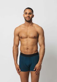 Männer Boxershorts aus tealfarbenem Baumwollmaterial mit einem schwarzen elastischen Bund. Sie bieten eine enge Passform und einen Fronttasche für Unterstützung. Glatte Textur.
