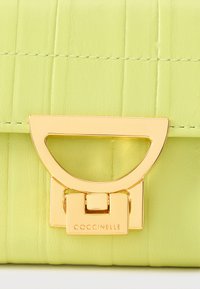 Zelená kožená kabelka s texturovaným povrchem, vybavená zlatým kovovým zapínáním a vyraženým logem, charakterizovaná čistými liniemi a strukturovaným tvarem.