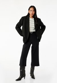 Blazer negro de gran tamaño sobre una blusa de rayas de color claro, combinado con pantalones cortos negros y botas de tacón alto hasta la rodilla.